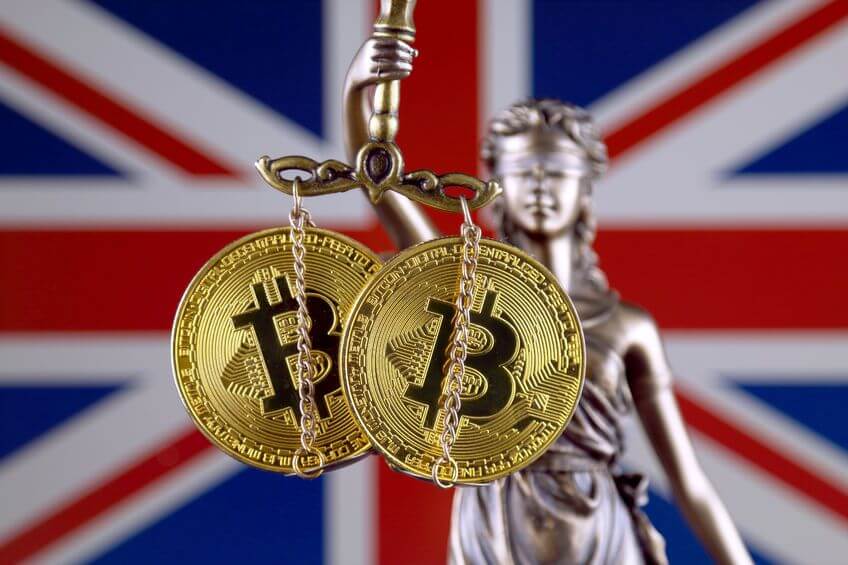 Imagen de la balanza de la justicia con las criptomonedas y la bandera de Reino Unido tras ella.